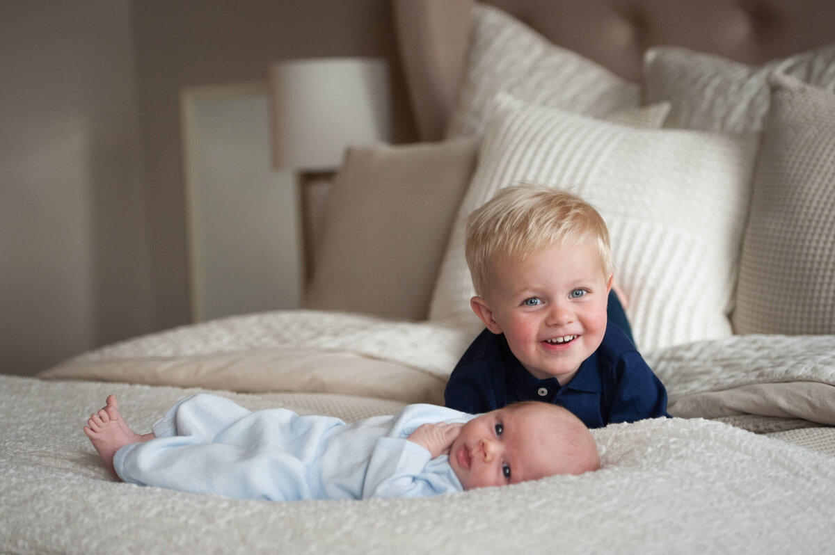 A toddler boy laying on a bed behind his newborn baby brother