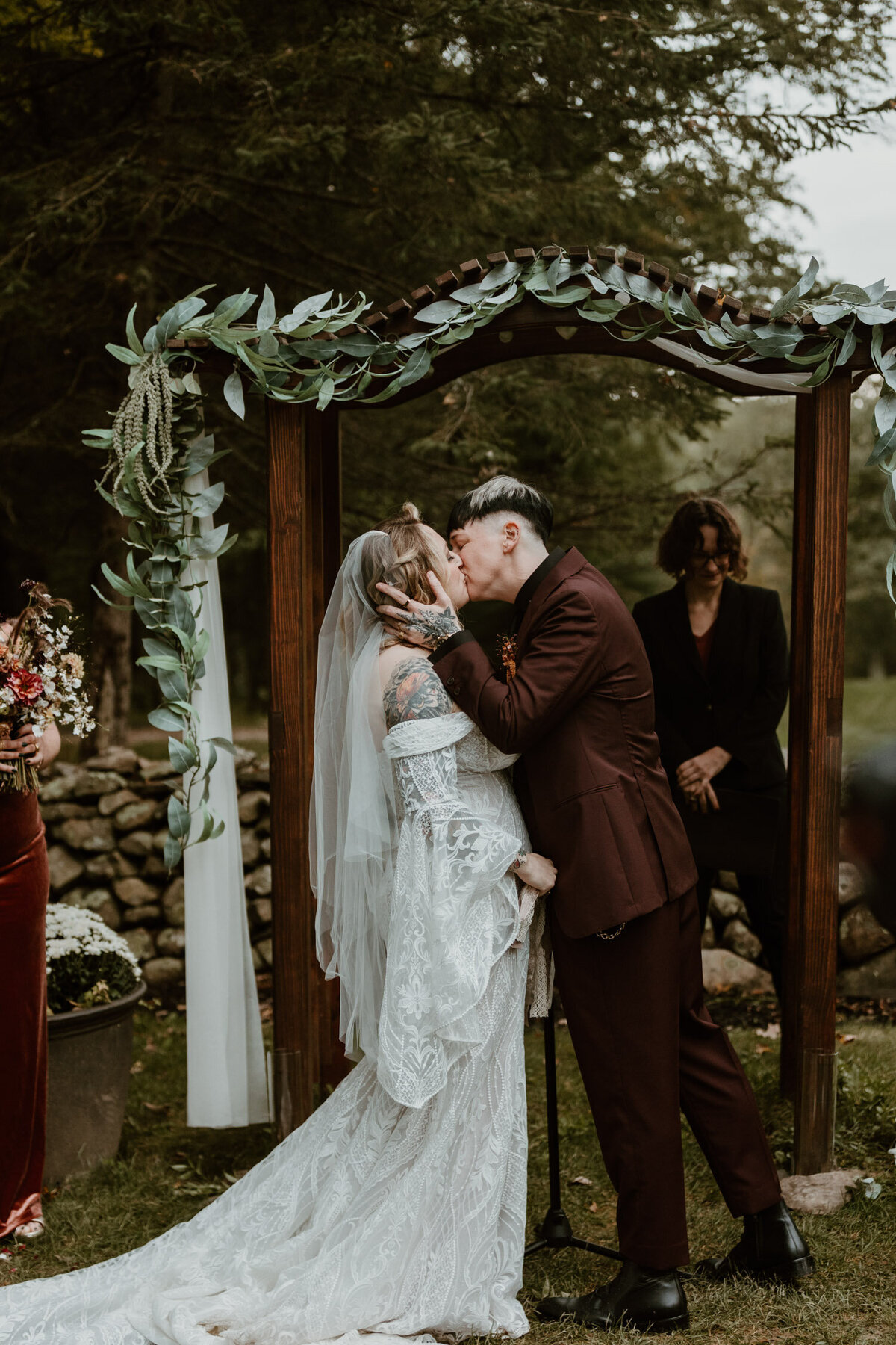 Bride and groom sharing an intimate kiss under a rustic wooden archway adorned with eucalyptus leaves, captured by a Hudson Valley wedding photographer.