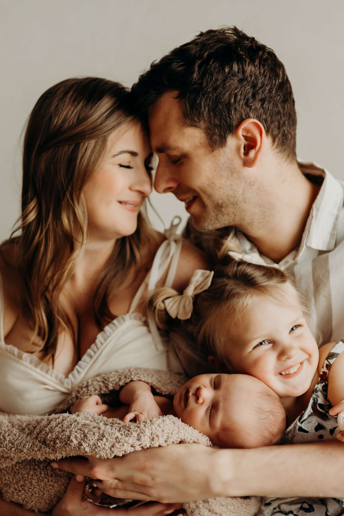 mom and dad laugh as big sister hugs her newborn brother