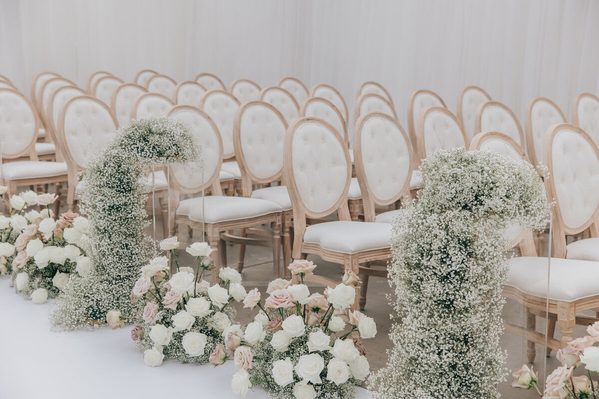 Ivory themed seating lined with baby's breath and roses at luxurious wedding ceremony