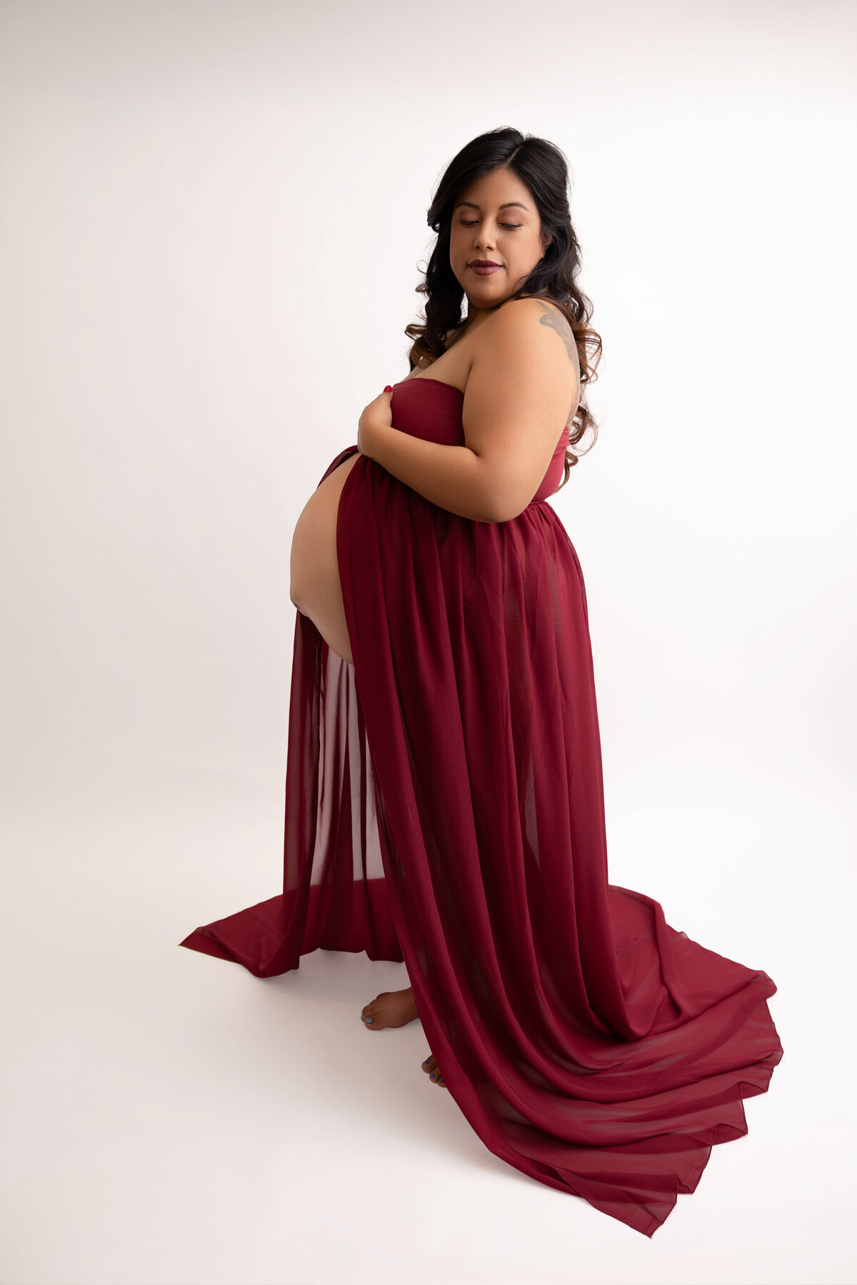 Pregnant mother wearing a burgundy dress showing pregnant belly. 