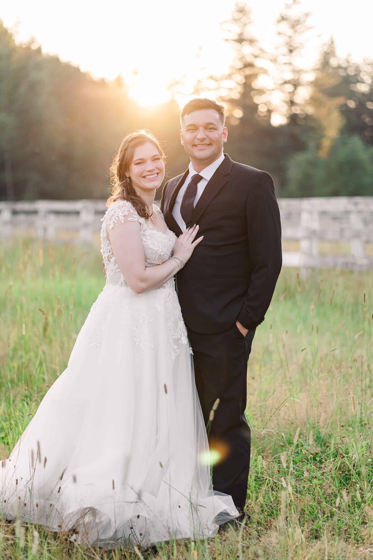 Bride and groom, standing in a field, facing the camera, during sunset at Rein Fire Ranch