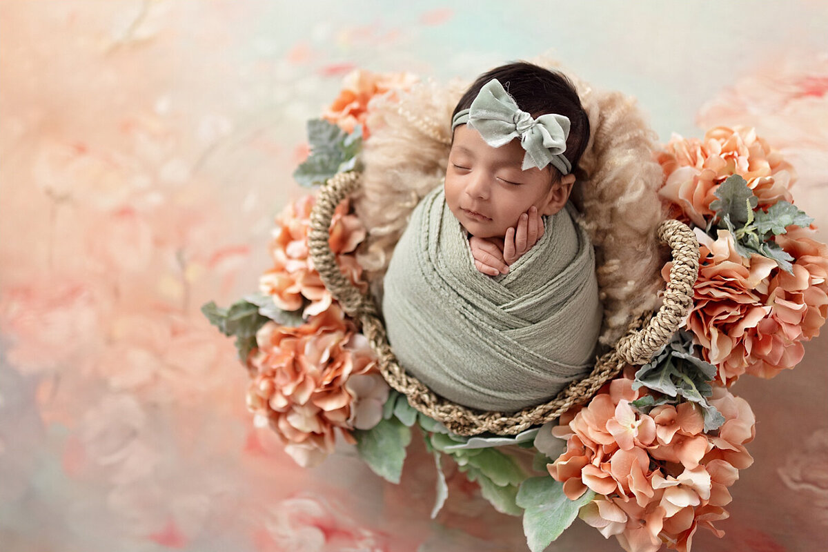Newborn baby girl wrapped in green posed among peach and coral florals in a botanical setup.