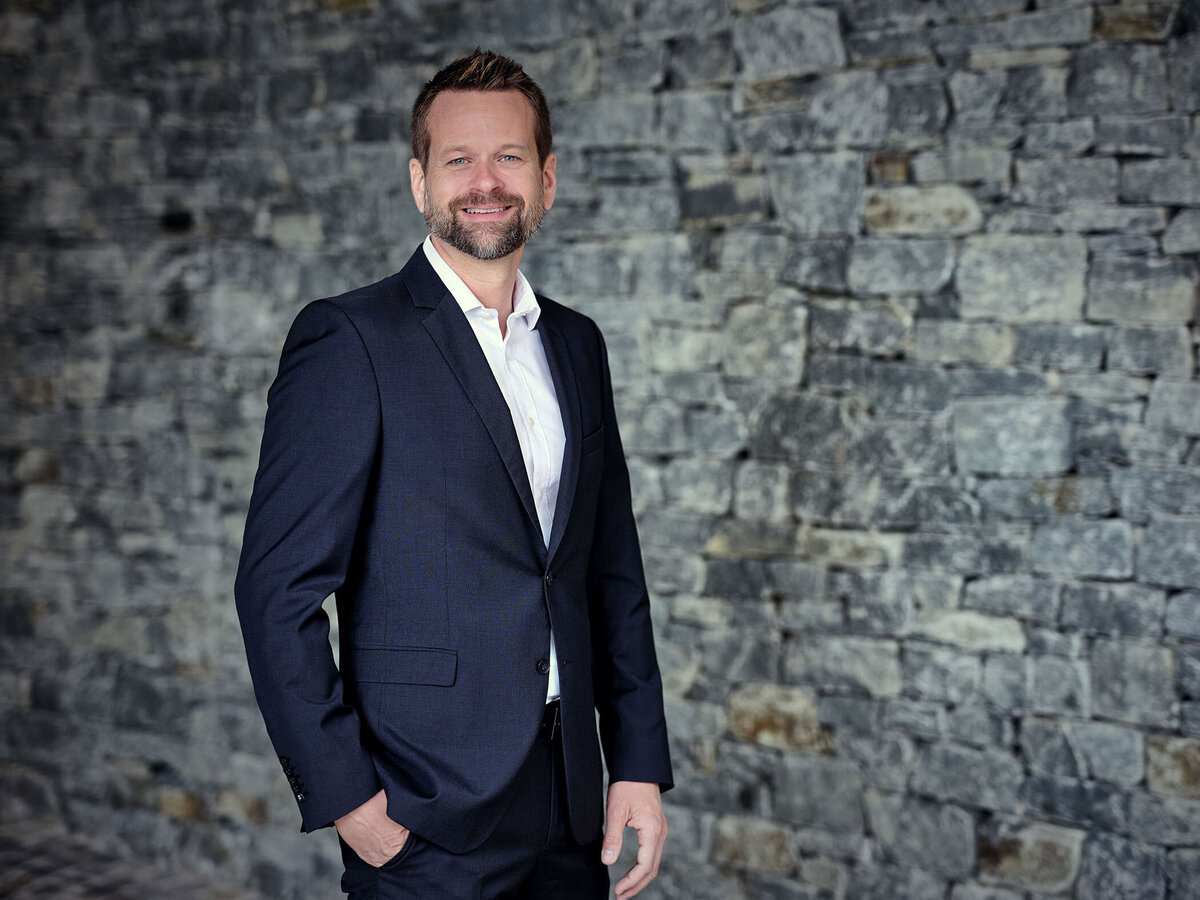 Professionelles Businessportrait im Freien vor einer Natursteinwand – aufgenommen von Atelier Schulte. Klare Bildsprache für persönliche Unternehmensdarstellung in ganz Österreich.