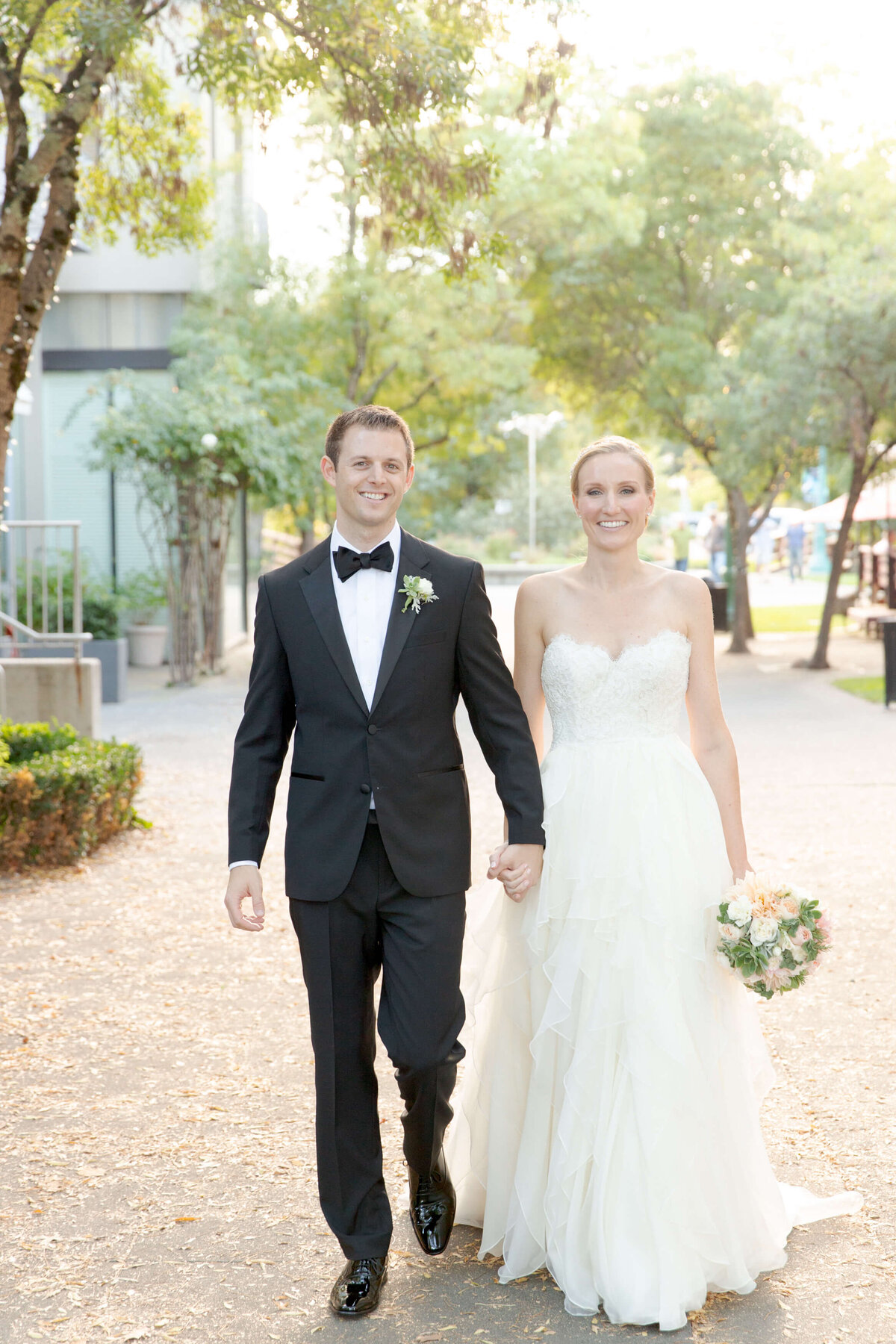 Newly married bride and groom hold hands and walk towards Robin Jolin's camera.