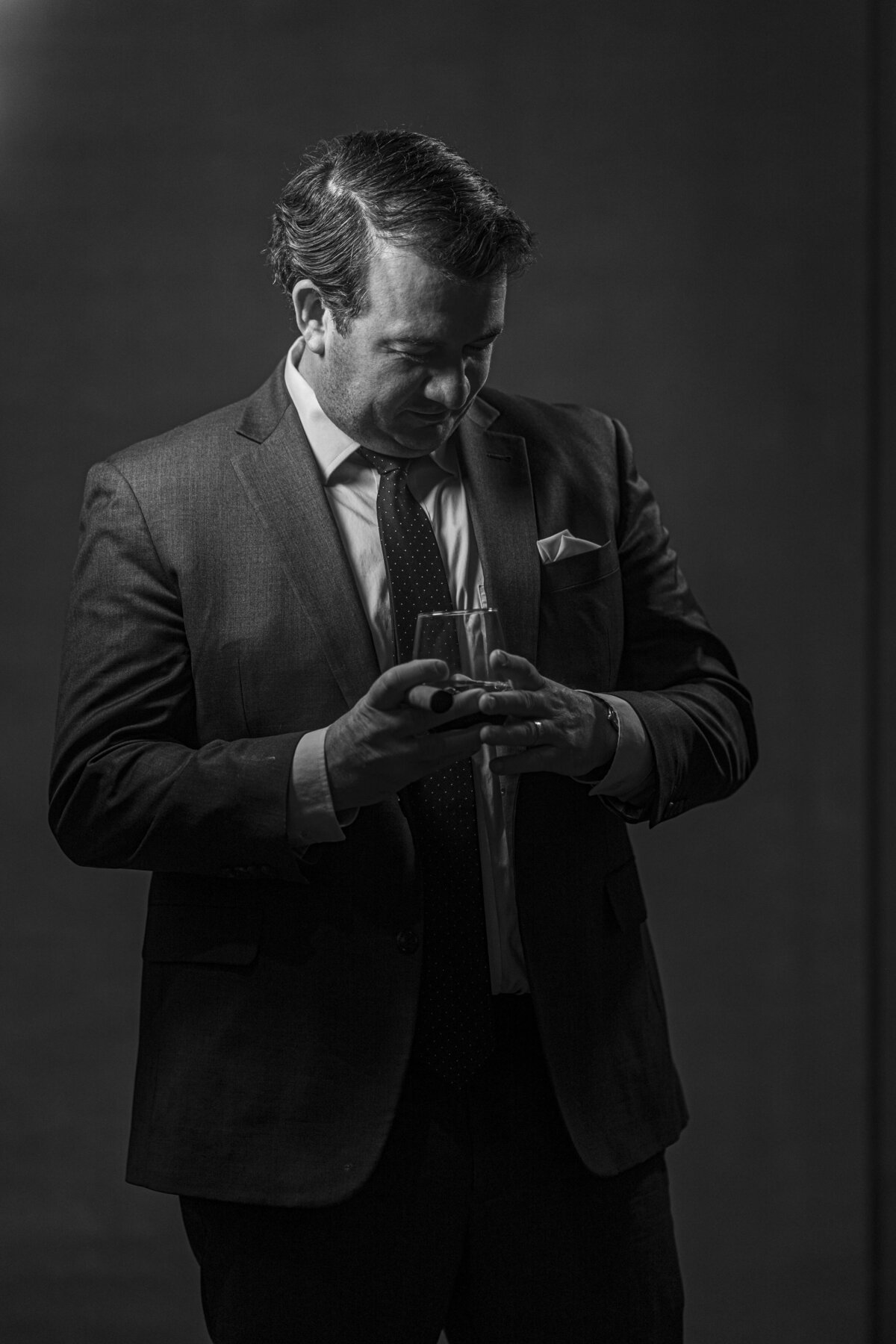 Black-and-white headshot in CT of man in suit adjusting tie, with dramatic side lighting by Rob Faber Photography.