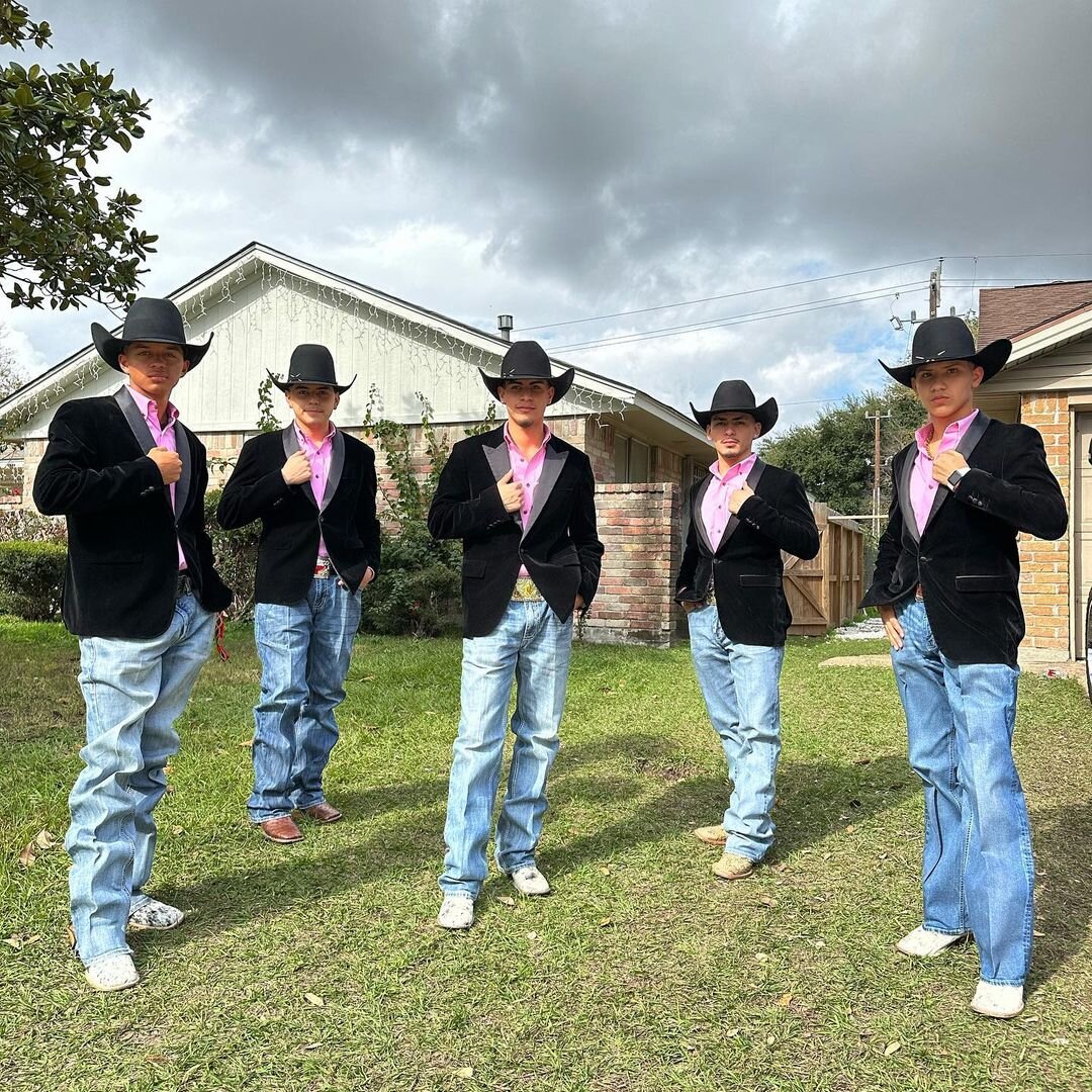 Three chambelones wearing cowboy hats, pink shirts, and black velvet Quinceañera suit jackets