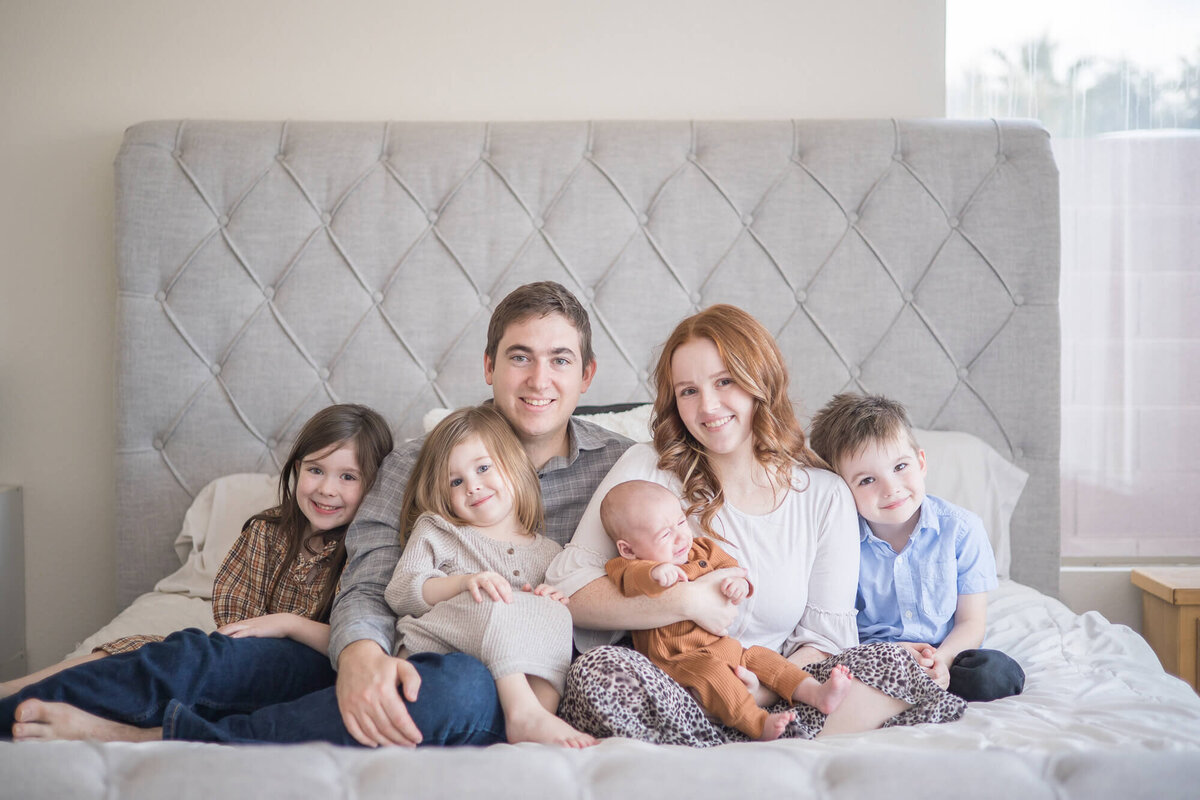 Family portrait of couple with three kids and a newborn on a bed