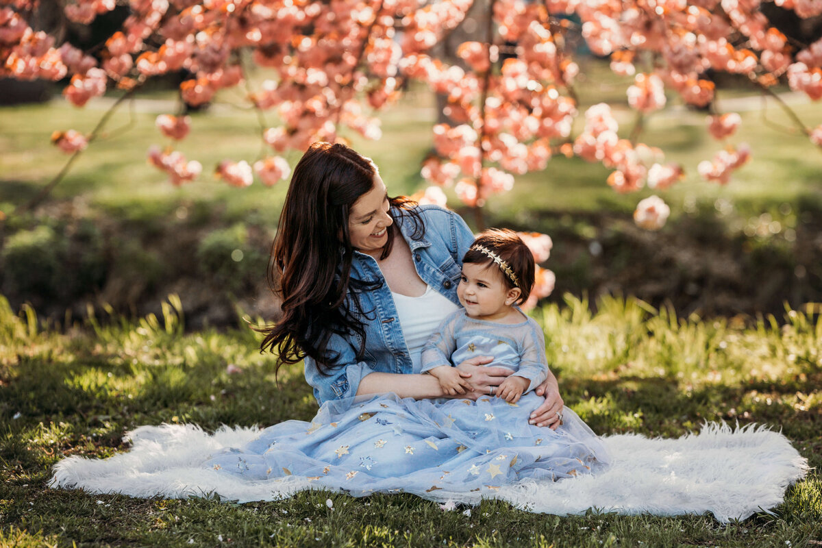 mother looking lovingly at her little grild surounded by spring flowers sitting in the grass