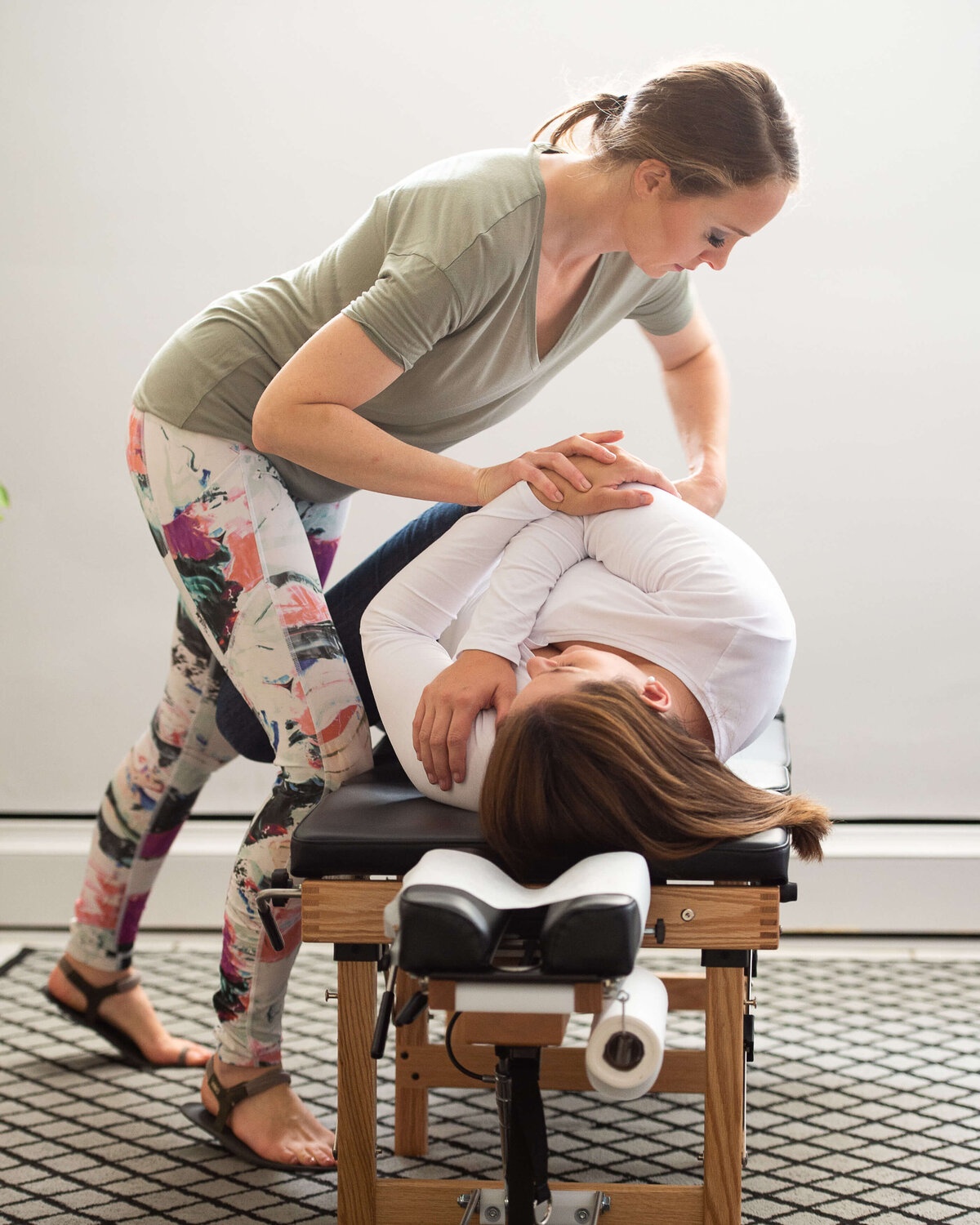 Ottawa branding photography showing a female chiropractor in a green shirt adjusting a female patient's spine on her bed.  Captured by JEMMAN Photography Commercial