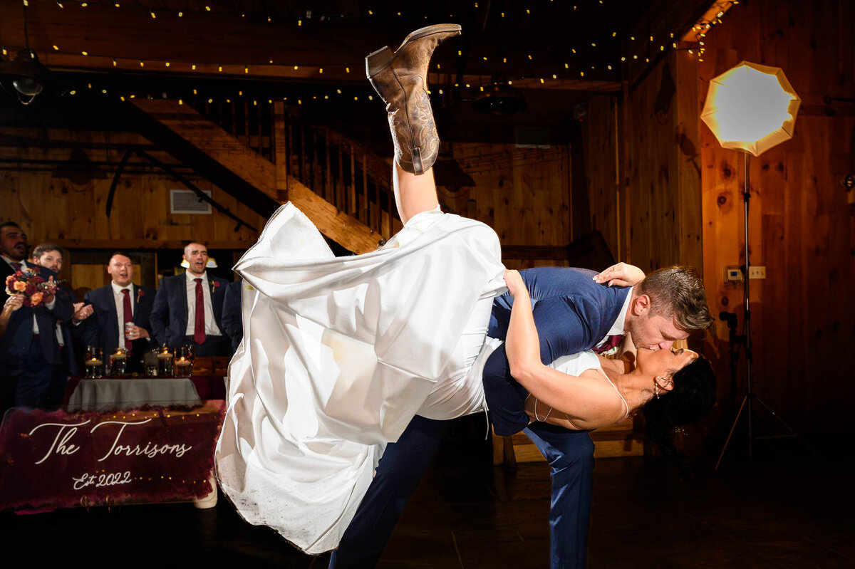 A bride kicks her cowboy boot in the air as her groom dips her and kisses her at their reception