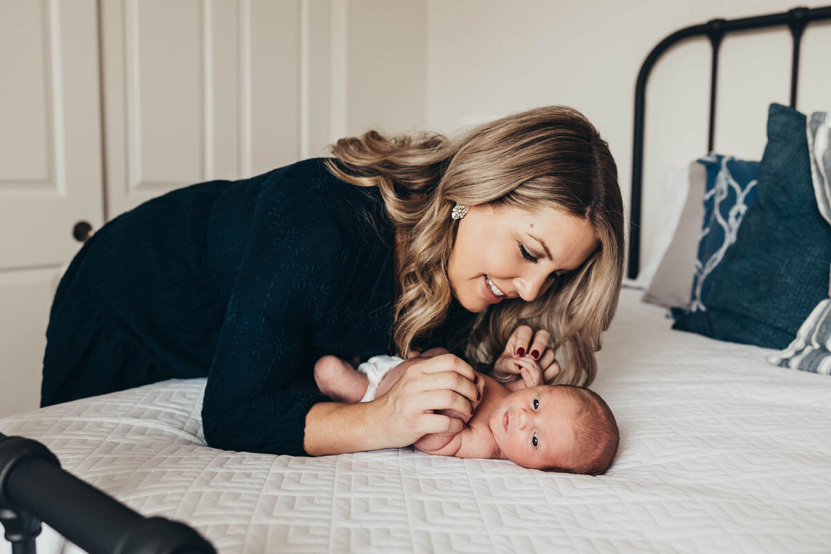 A mother leans over her sweet newborn baby lying on a bed in their Chula Vista home