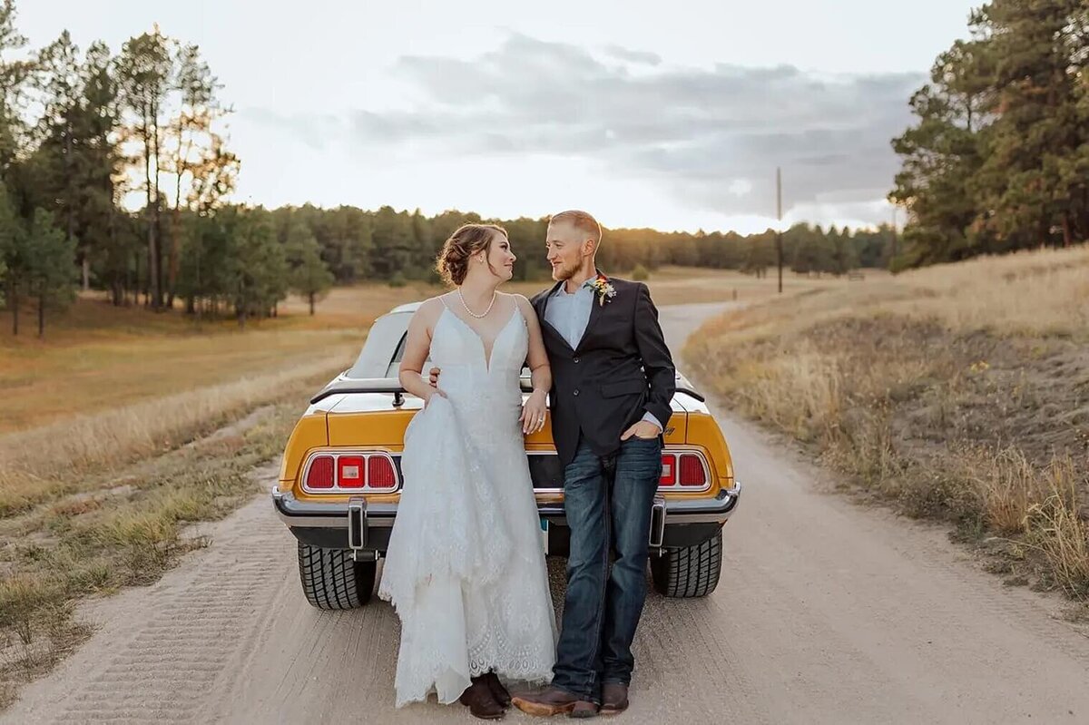 Bride and groom looking at each other leaning on sports car. Photographed by Colorado Wedding Photographer