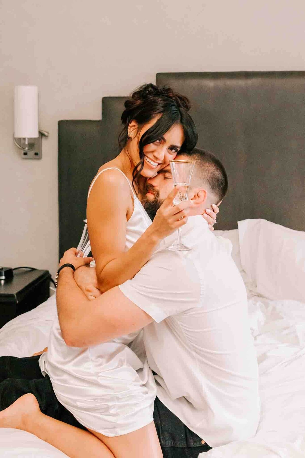 bride sits on grooms lap while he holds her, and she holds a champagne glass, at Hotel Icon.