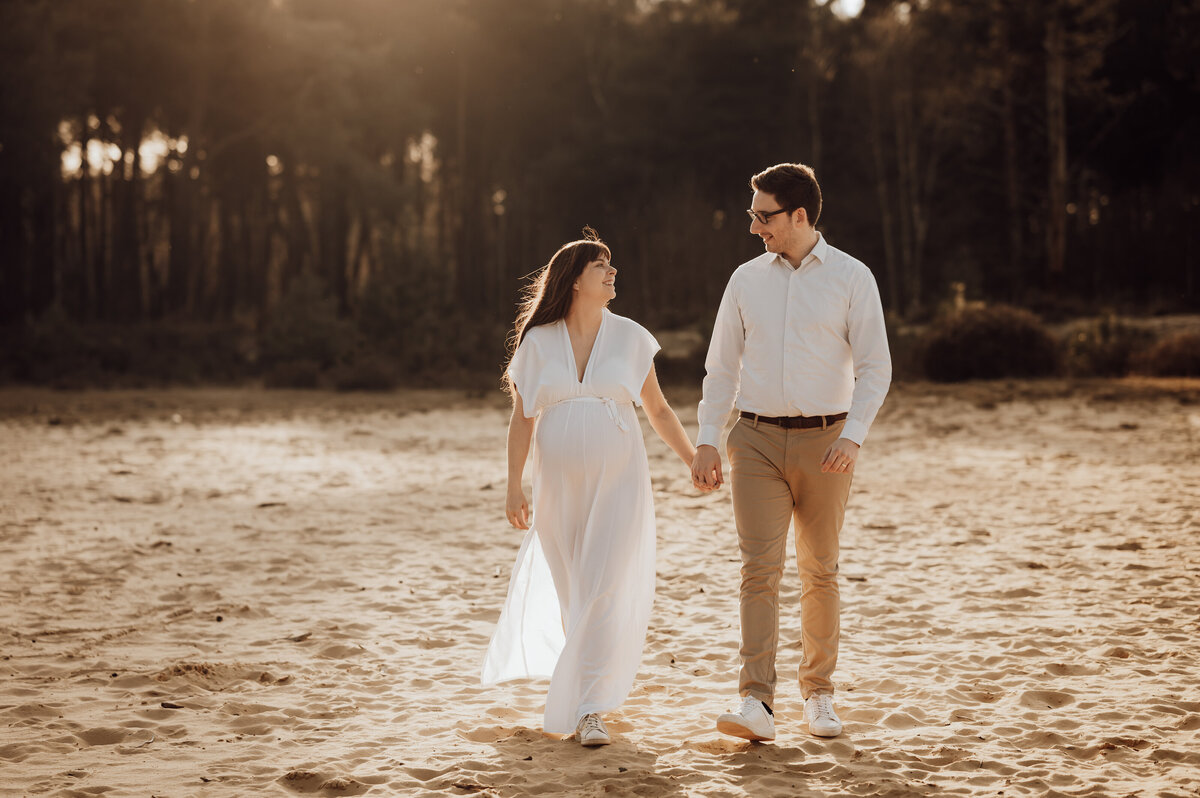 Koppel kijkt elkaar liefdevol aan elkaar tijdens zwangerschapsshoot op de heide in Antwerpen