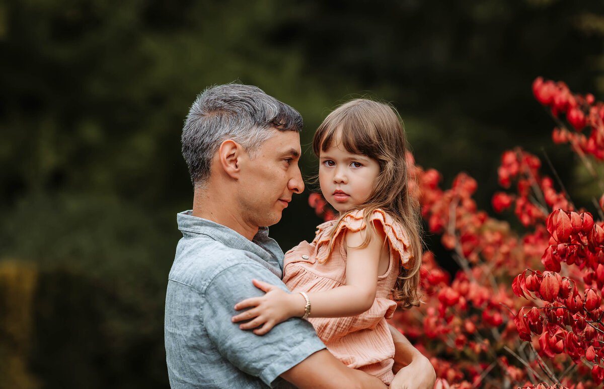 Father holding his daughter at Kubota Garden in Seattle, gazing at her with love during a tender family moment.