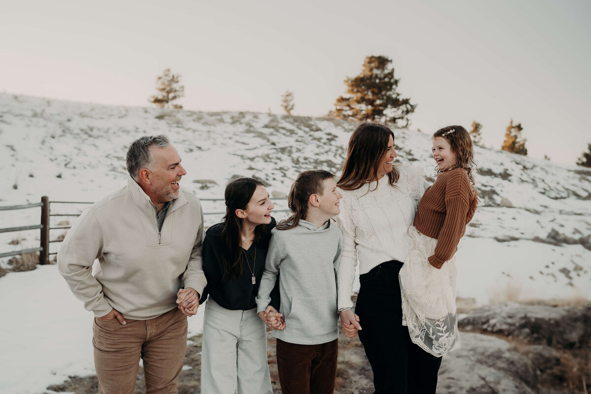 A family of five walks on a trail, surrounded by beautiful snowy hills and a gorgeous old fence, while dressed fashionably in Brown's and creams to coordinate with the winter backdrop.