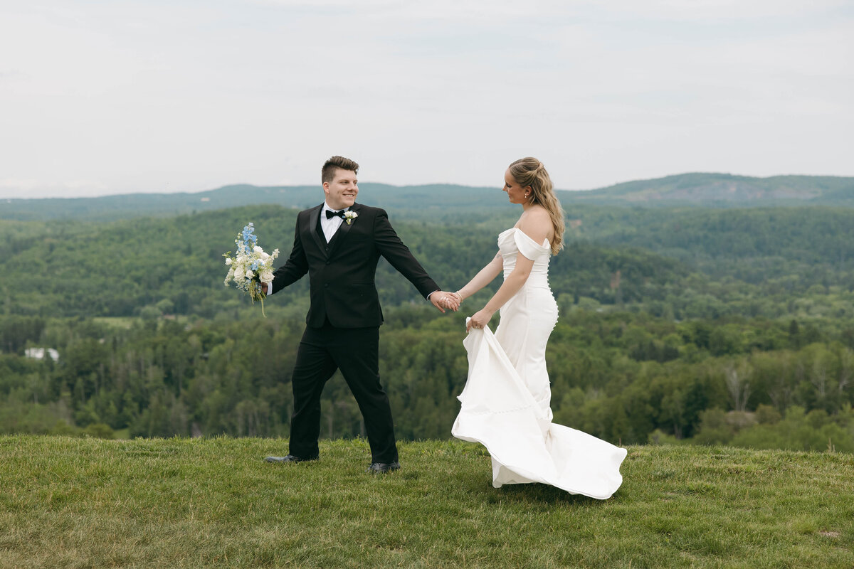 bride and groom walking with mountains behind them, groom is in a black tux and the bride is in a timeless wedding gown with buttons going down the back. Oahu Hawaii Wedding Ceremony, Green mountains in the backgorund