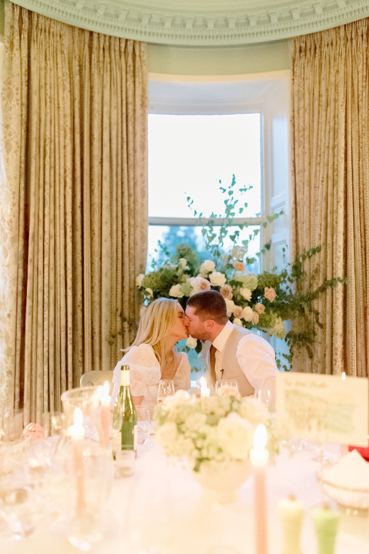 Bride and Groom kiss with abundant wedding florals by Lavender and Rose Events and candlelit tables with pink taper candles in Cromlix House country house wedding venue Scotland.