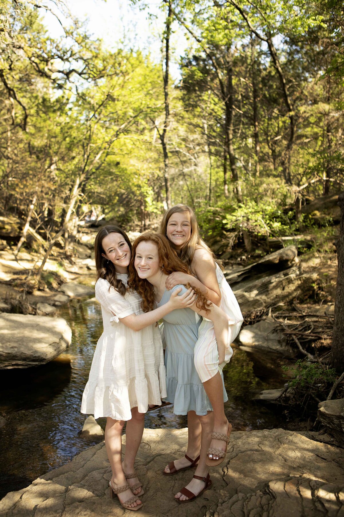 Sisters laughing and playing by the creek in Flower Mound, capturing a joyful moment during their photoshoot