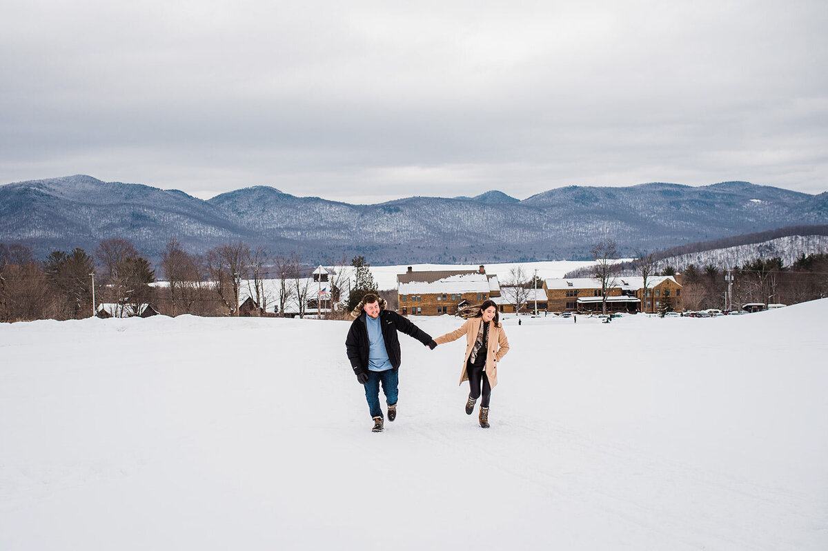 engaged couple running in snow in winter mountain top inn vermont