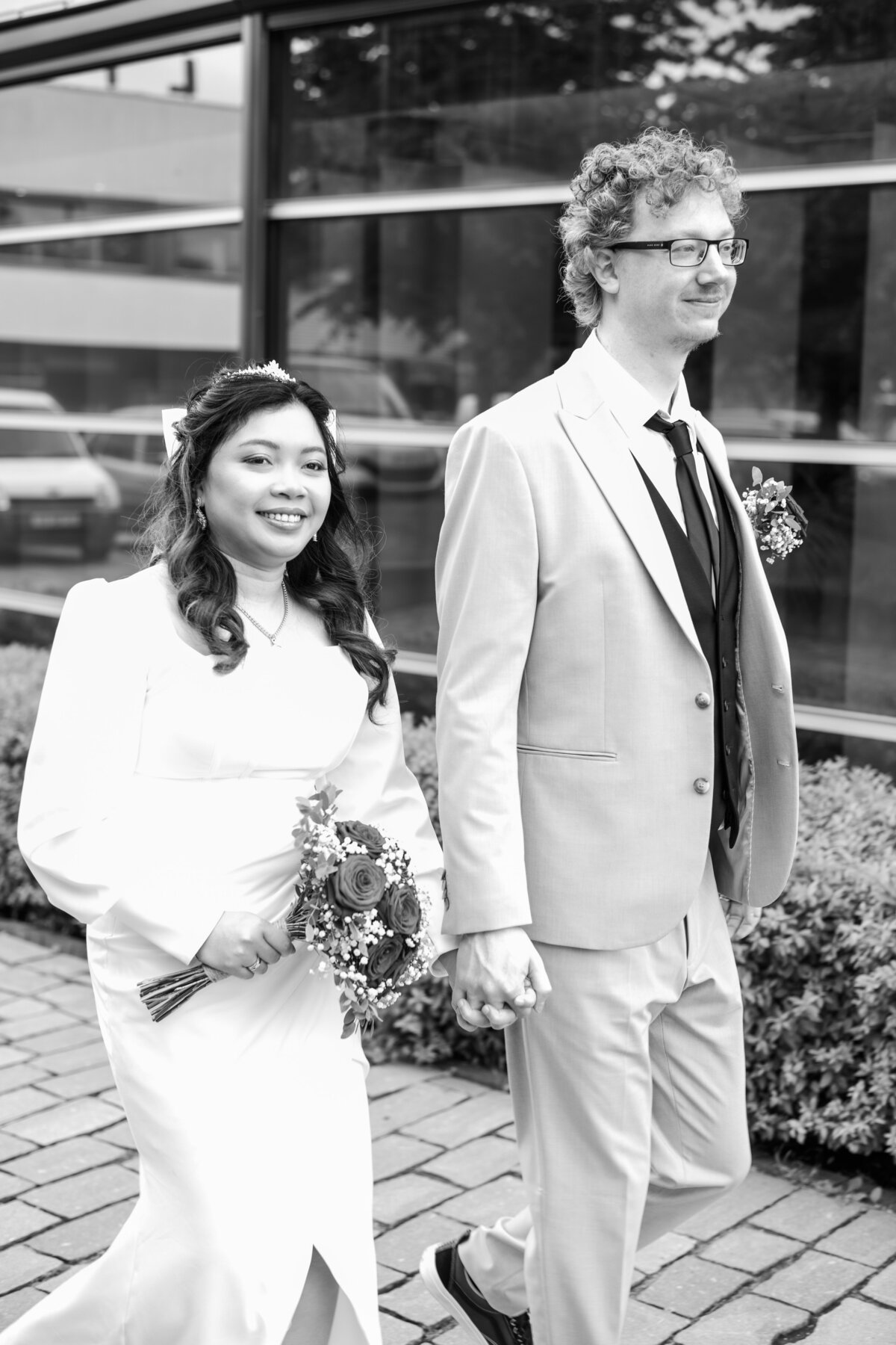A bride and groom walk hand in hand in a black and white photo after their wedding in the gemeentehuis in Veldhoven