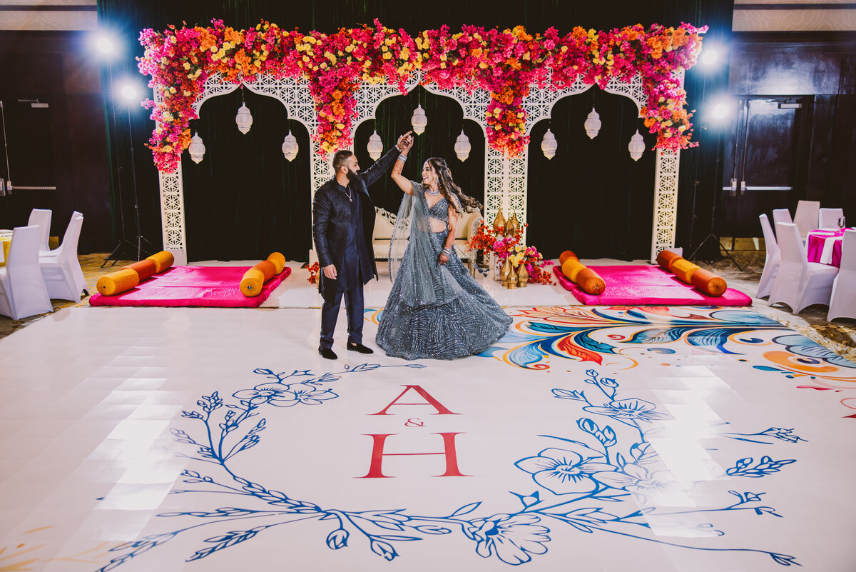 Groom twirling bride inside the dance floor at a decorated sangeet ballroom during their indian wedding week