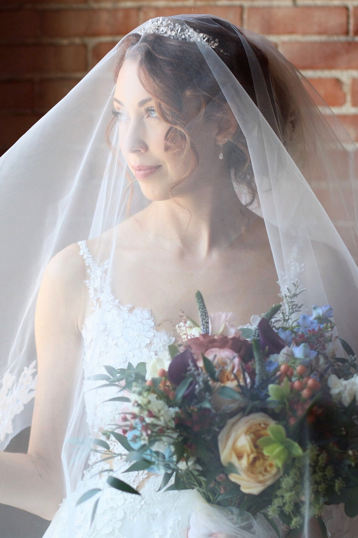 Bride with veil over her face looking out window holding spring flowers at Monarch KC