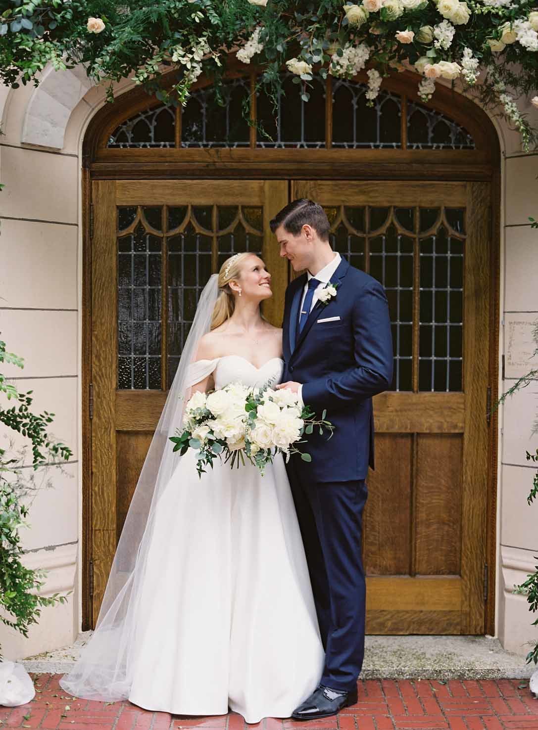 bride and groom in front of the Villa Academy chapel with floral arch around entrance doors