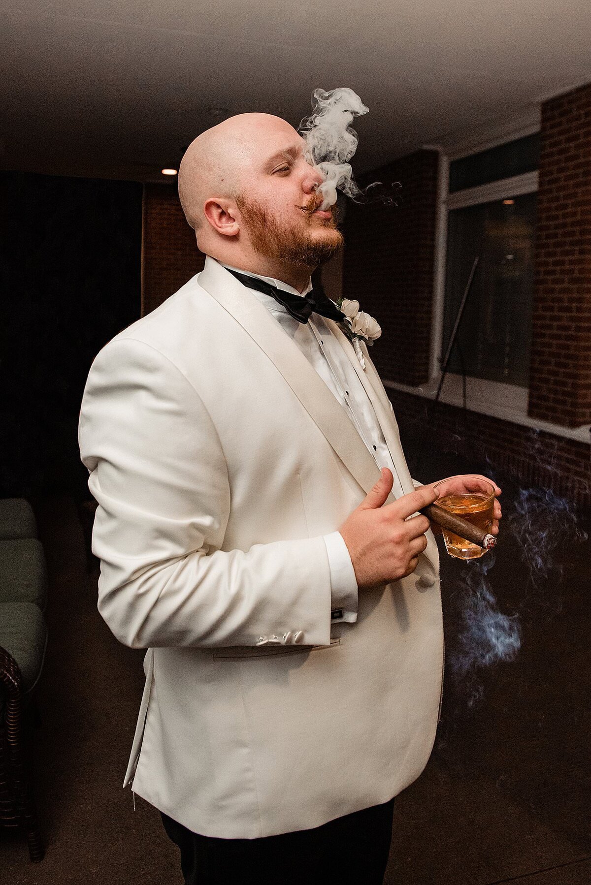 Groom in a white dinner jacket laughing alongside one of his groomsmen wearing a black jacket and bow tie