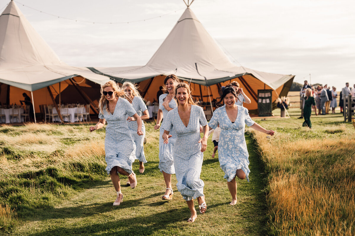 Bridesmaids running from wedding tent in field