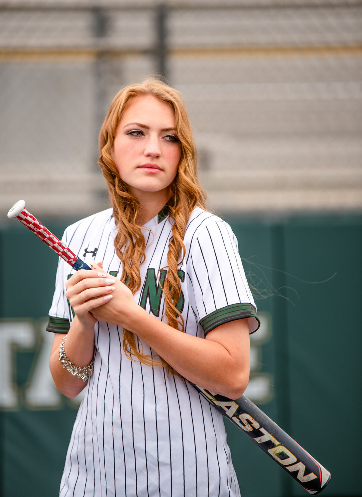A Santa Fe graduate stands near home plate holding her bat and looking off to her left.