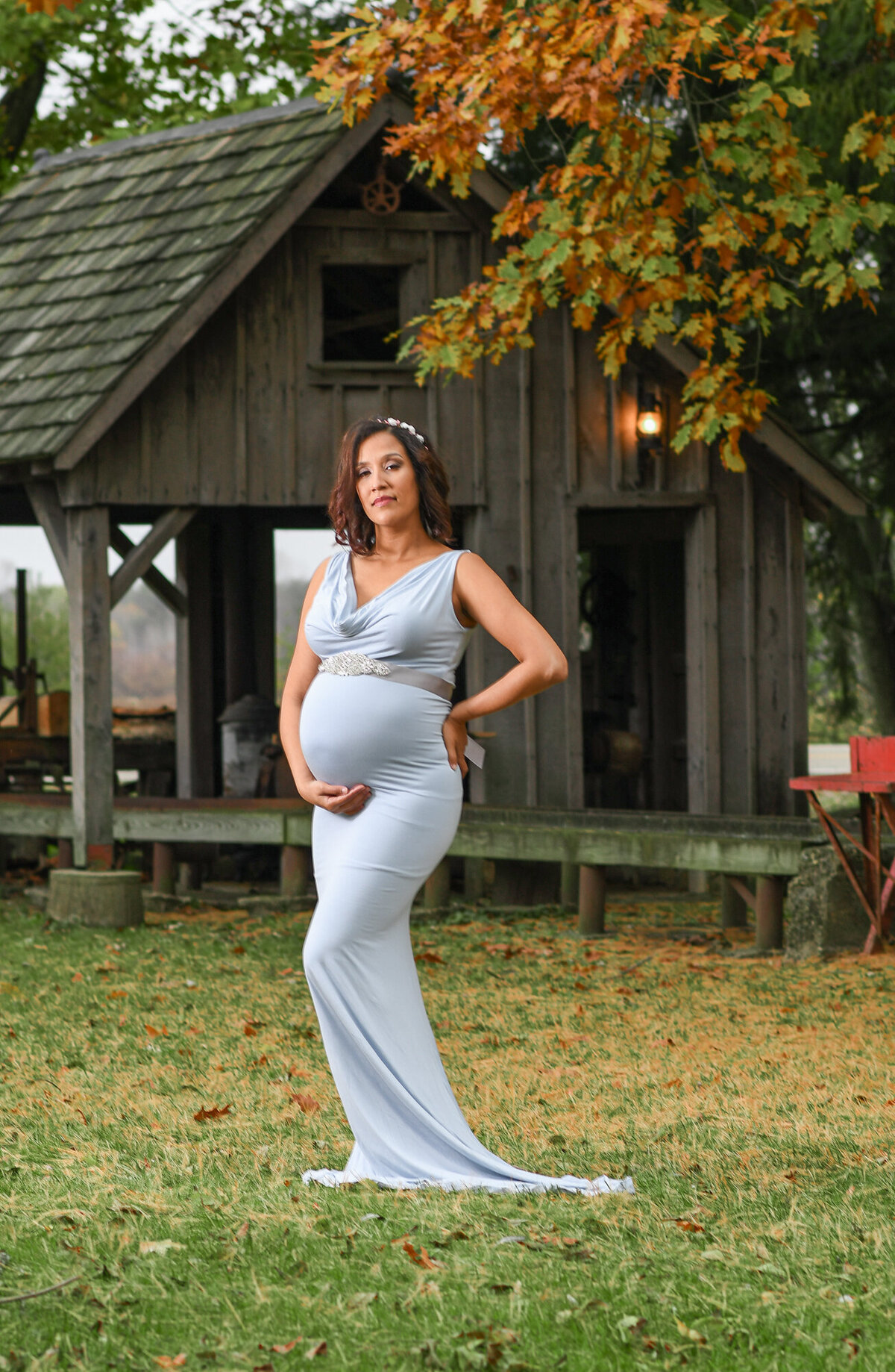 Pregnant woman in a beautiful long maternity gown outside by a rustic building