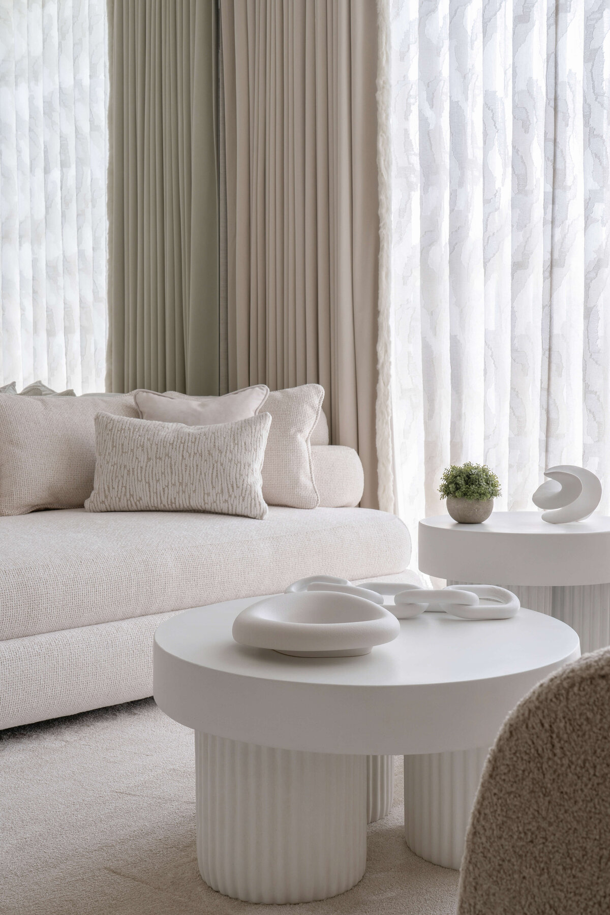 A white couch and contemporary white coffee table adorned with white decor in the sitting area of a light, neutral primary bedroom.