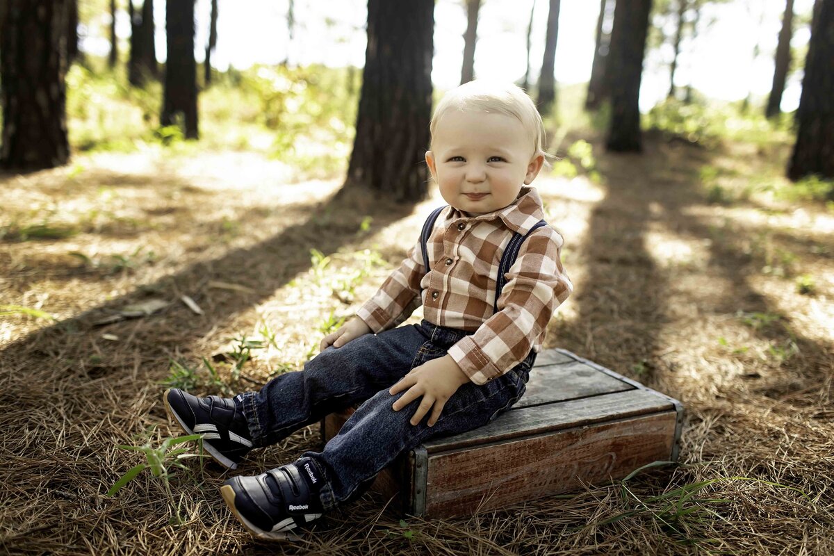 Smiling birthday boy in suspenders and overalls, enjoying the outdoors surrounded by tall pine trees