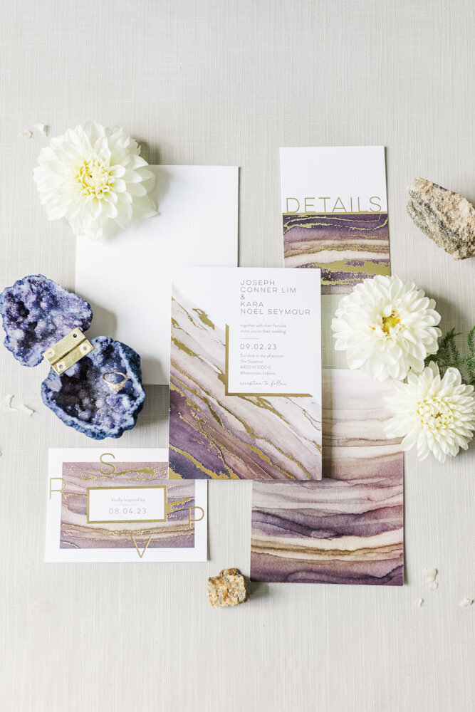 a flat lay of wedding invitations with flowers and a ring box