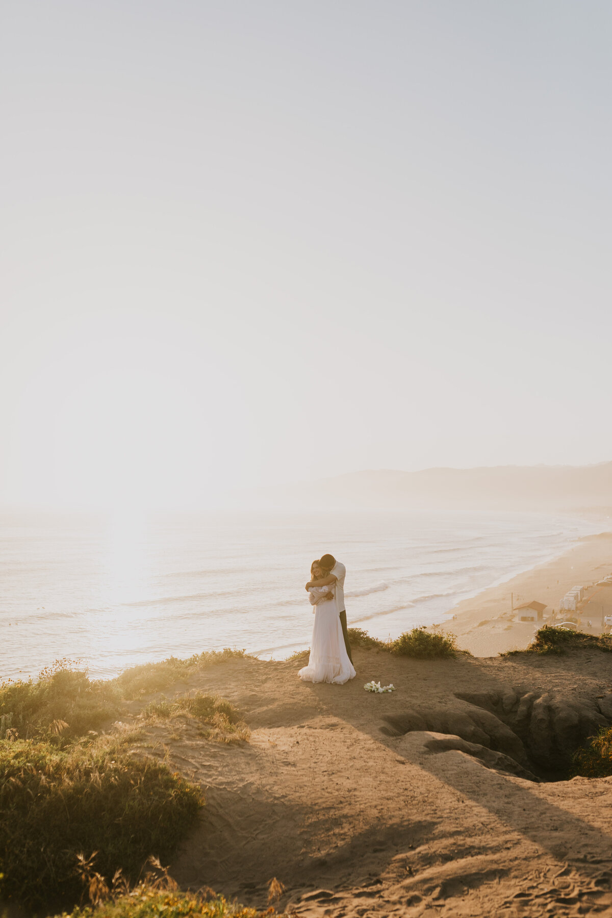 Bride standing alone on a sandy shore, serene wedding portrait.