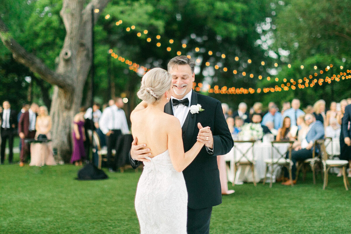man in black tuxedo dancing with bride at green garden wedding reception
