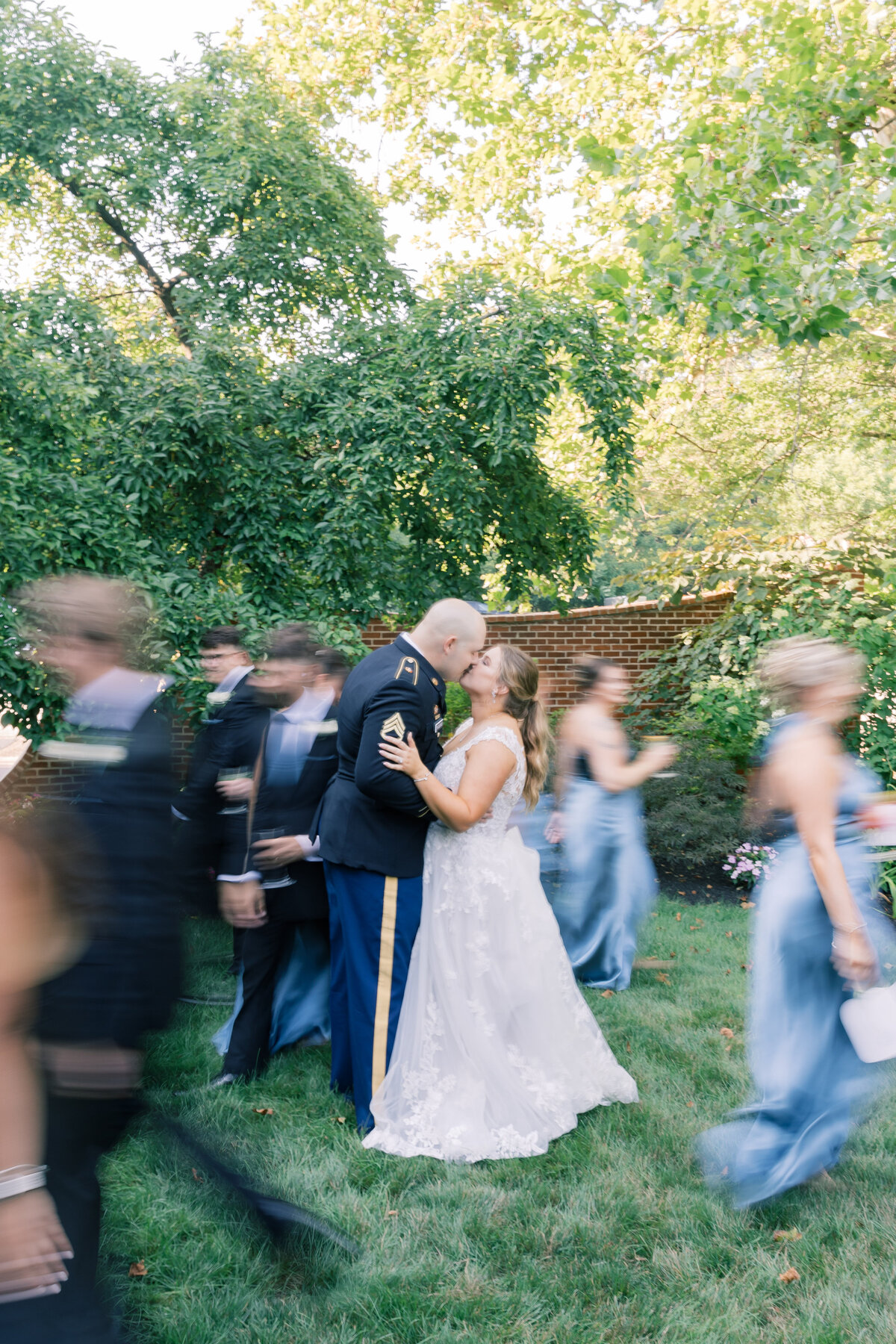 Wedding couple kissing at Stone Mill Manor with their bridal party walking past, capturing a joyful celebration.