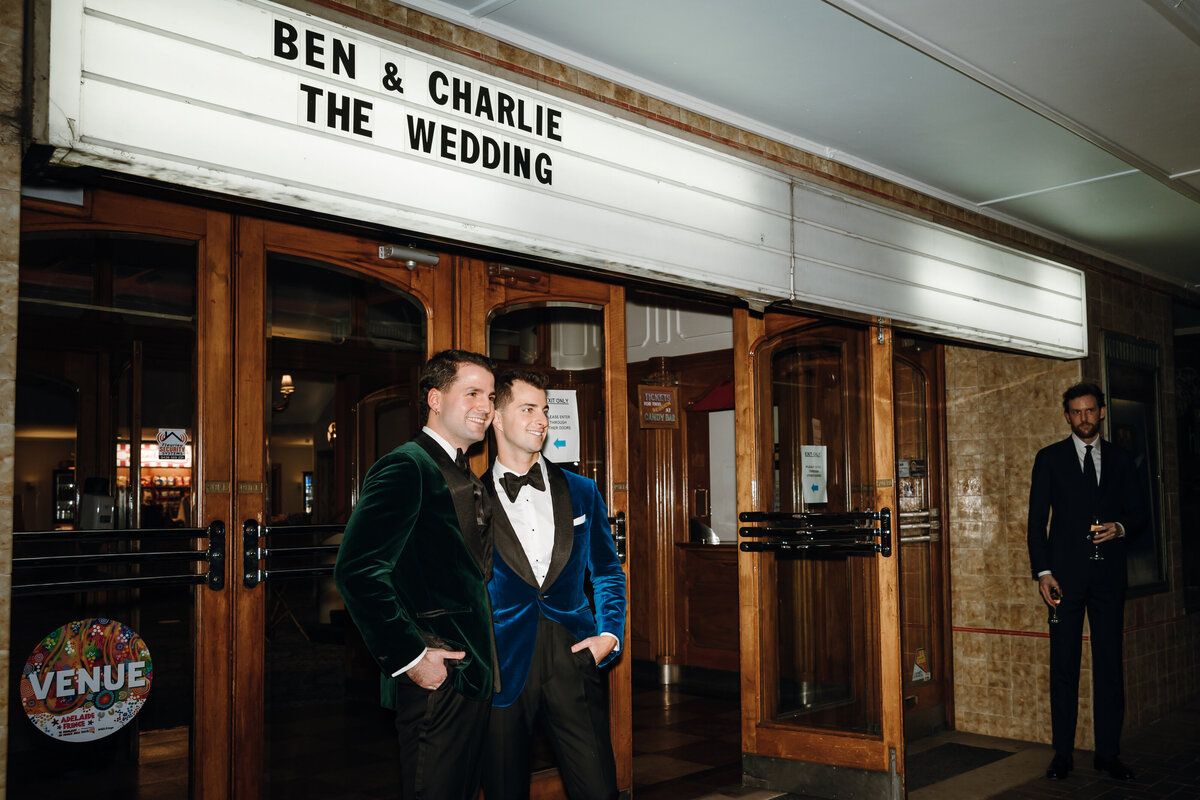 The grooms in green and blue velvet suits outside the entrance of regal cinema.