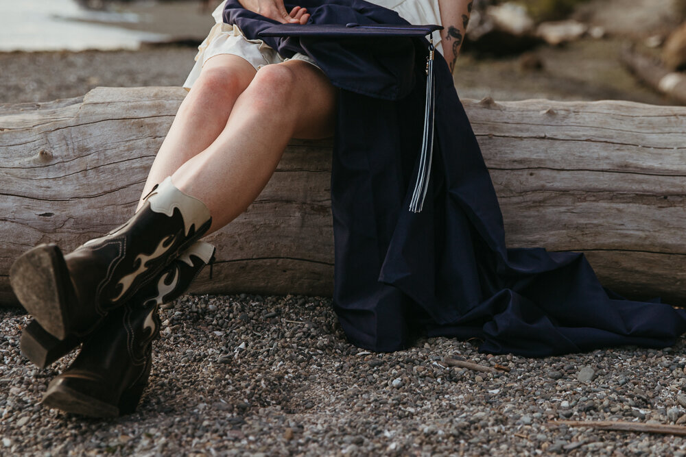 Close up of a girl on the beach with her cap and gown sitting on a log