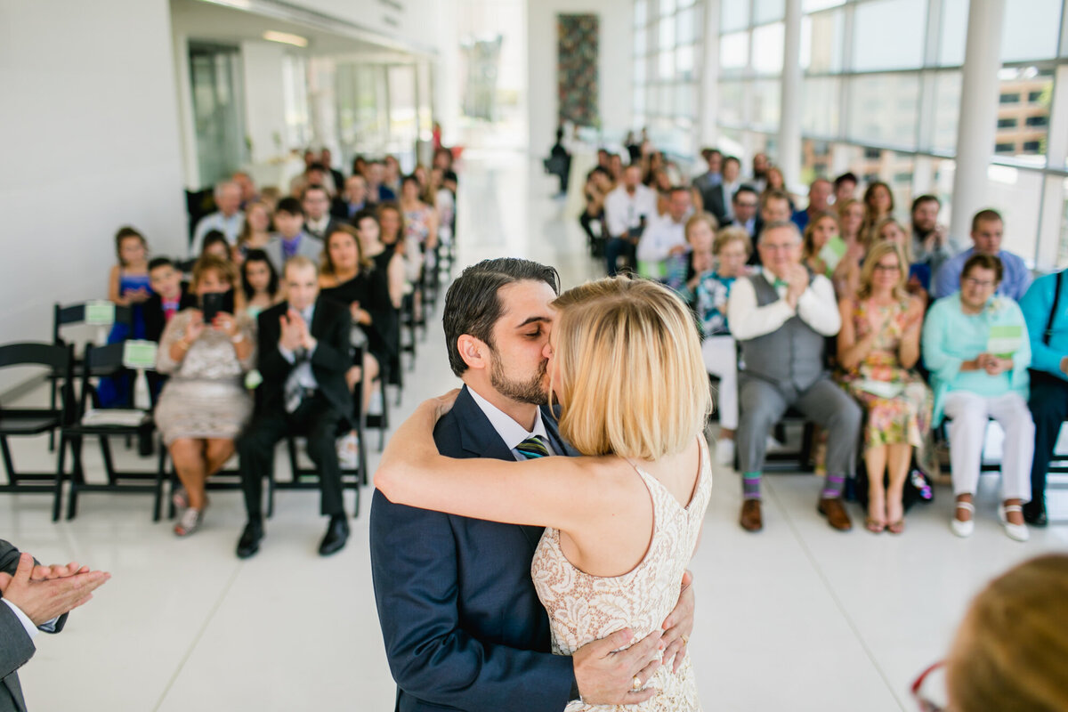 Bride and groom kiss at the end of their wedding ceremony while guests look on