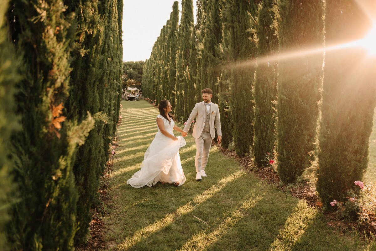 Brautpaar laufend in einer Allee aus Zypressen