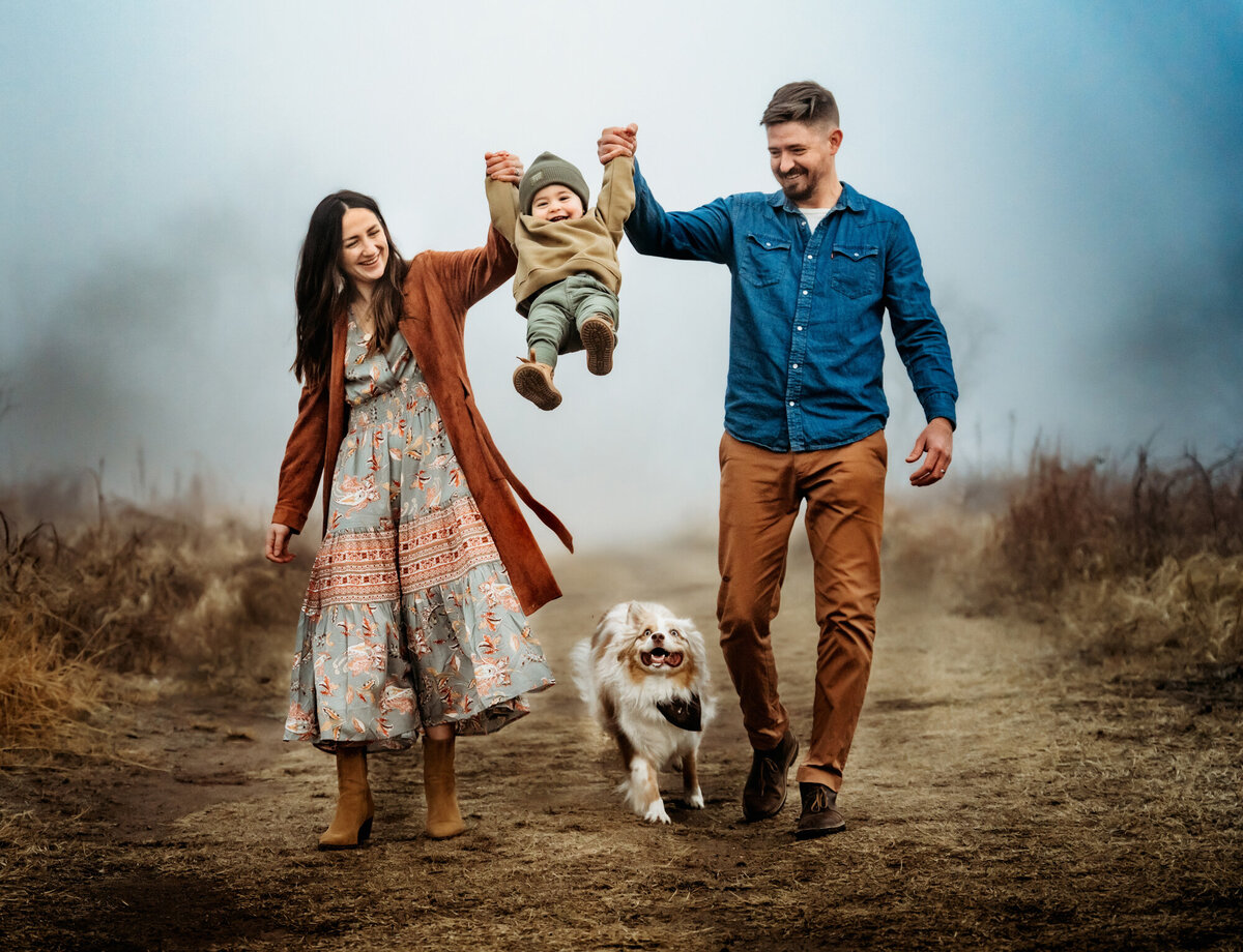 Family Photographer, Mom and dad swing their son outside as their do walks beneath him