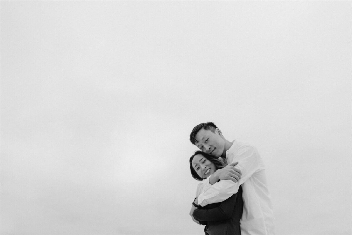 Black and white photo of a man lovingly hugging his fiancee in Fire Island Beach, NY. Engagement Image by Jenny Fu Studio