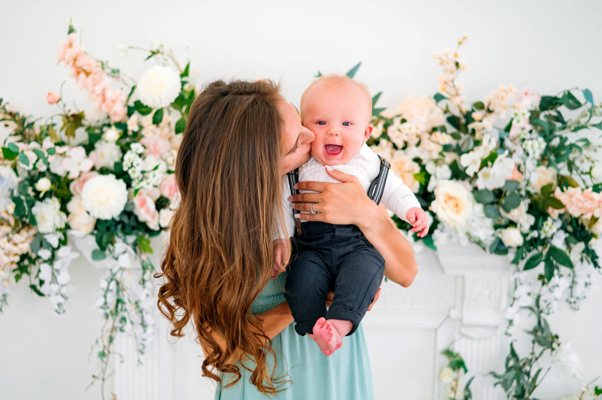 Mother holding her baby surrounded by floral backdrops during a motherhood portrait session in Plano, Texas, photographed by Jennifer L. Kirk Photography.
