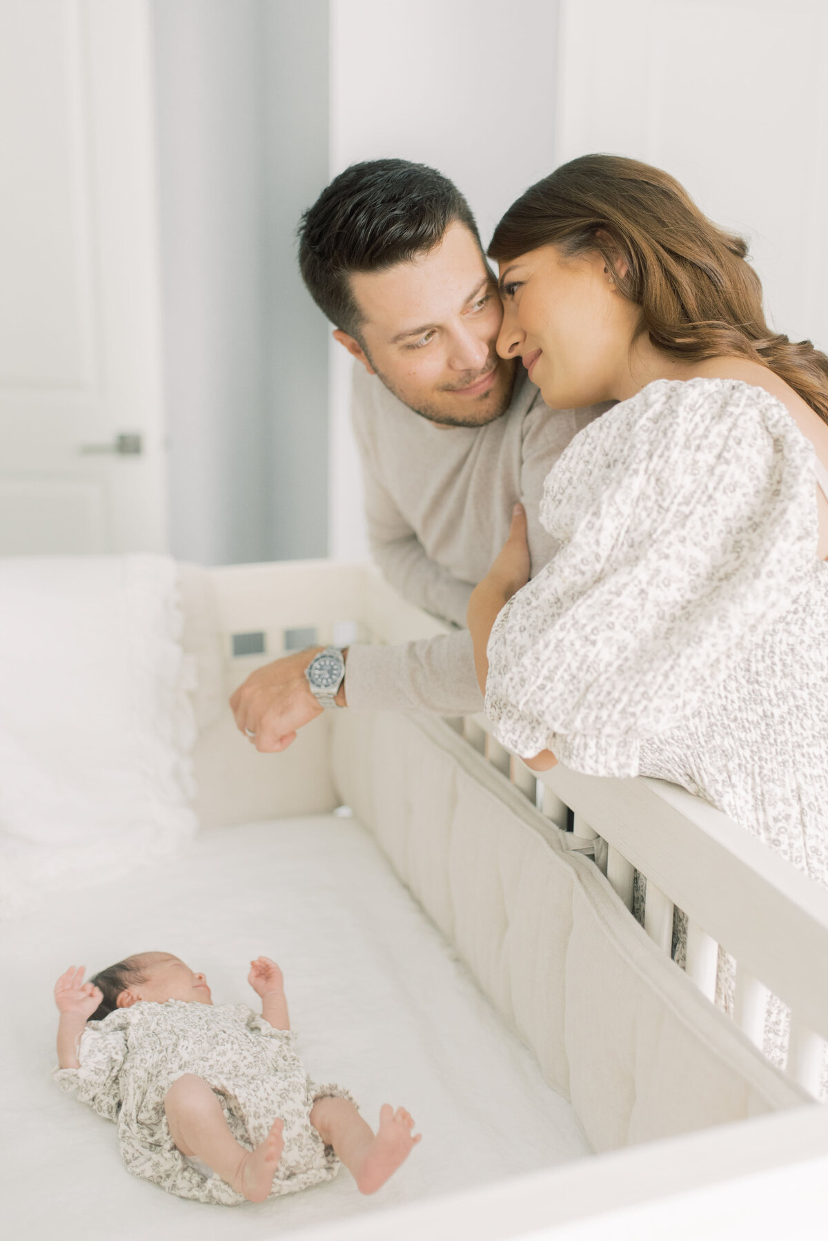 Parents leaning in over crib as their baby sleeps – loving gaze between partners in a peaceful nursery