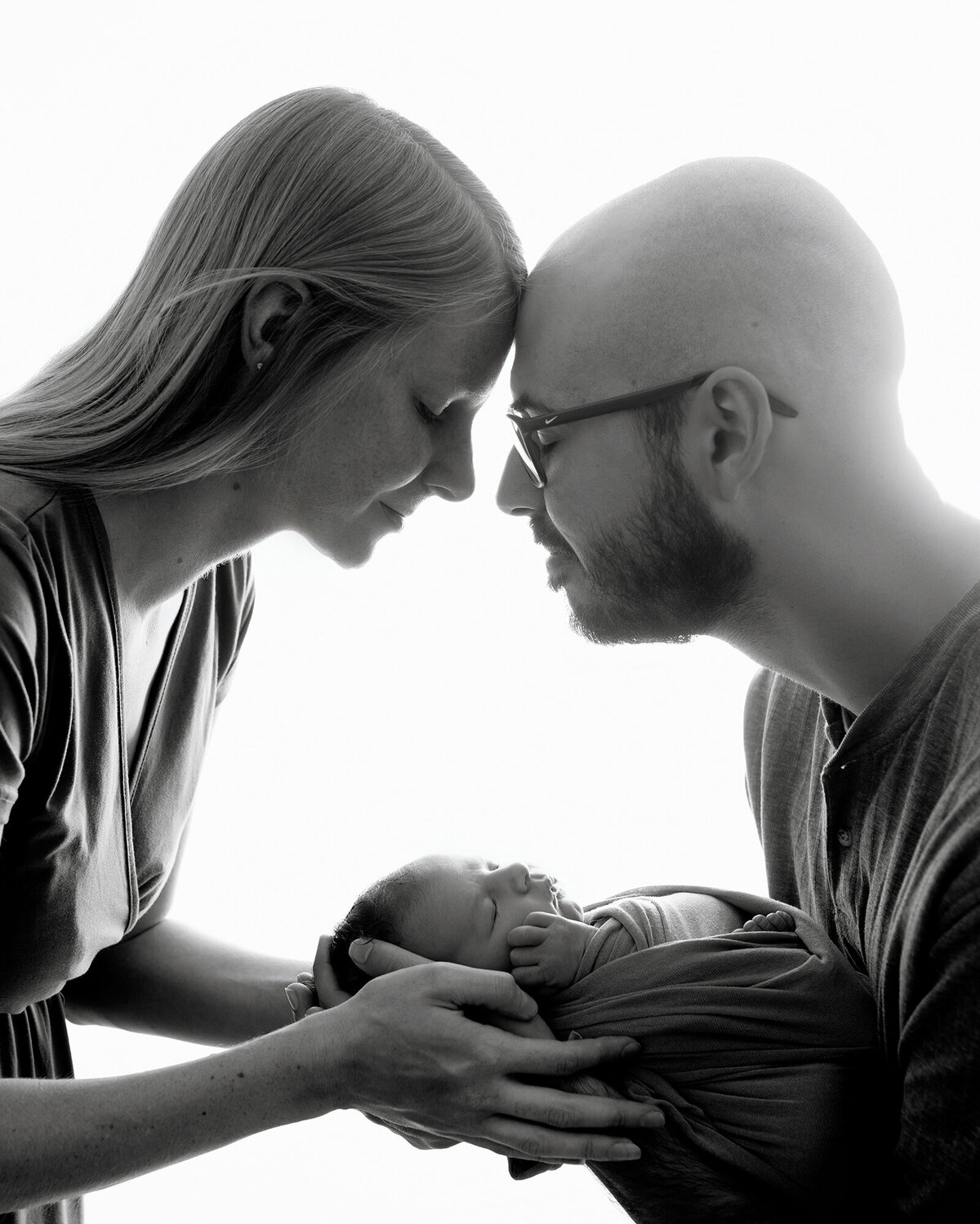 Happy parents touch foreheads over their newborn in their hands