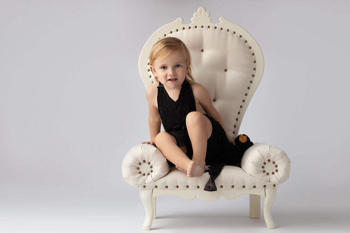Toddler sitting on a vintage chair with a stuffed bear, captured by a family photographer in Dallas.