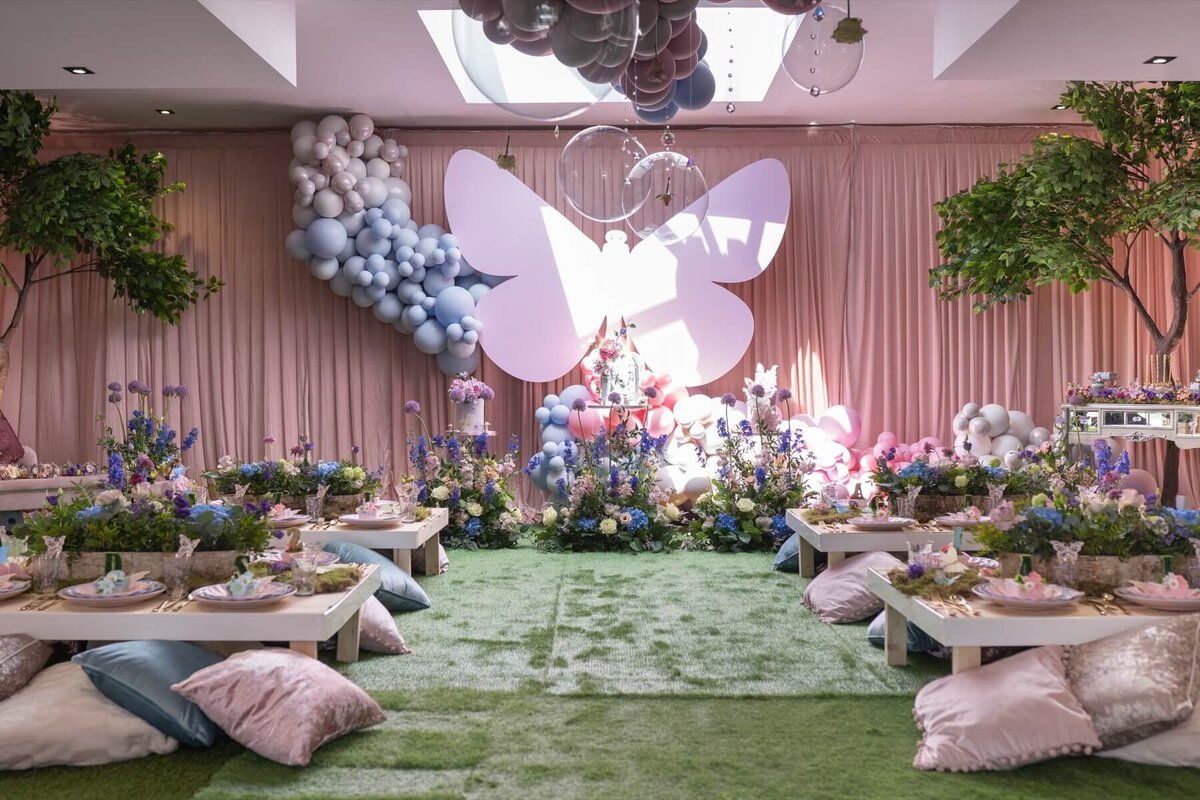 Children's garden party setting with low tables and velvet cusions with grand florals, balloons and butterfly decorations